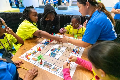 A group of elementary age boys and girls play a board game.